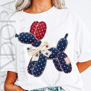 May include: White t-shirt featuring a patriotic balloon dog design. The dog is crafted from patches of red and blue fabric, adorned with white stars. A cream-colored bow adds a decorative touch. The design is stitched onto the shirt.