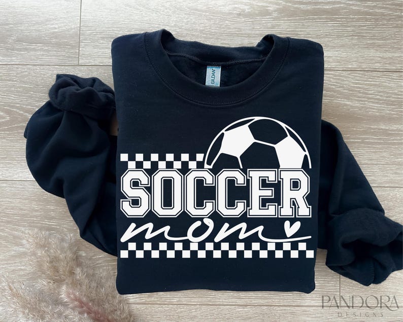 Pu&ograve; includere: Felpa nera con una grafica di pallone da calcio bianco e il testo "Soccer Mom" con un cuore.