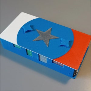 Puede incluir: Una baraja de cartas azul, blanca y naranja con un dise&ntilde;o de estrella en la parte superior. La baraja est&aacute; hecha de pl&aacute;stico y tiene un borde redondeado.