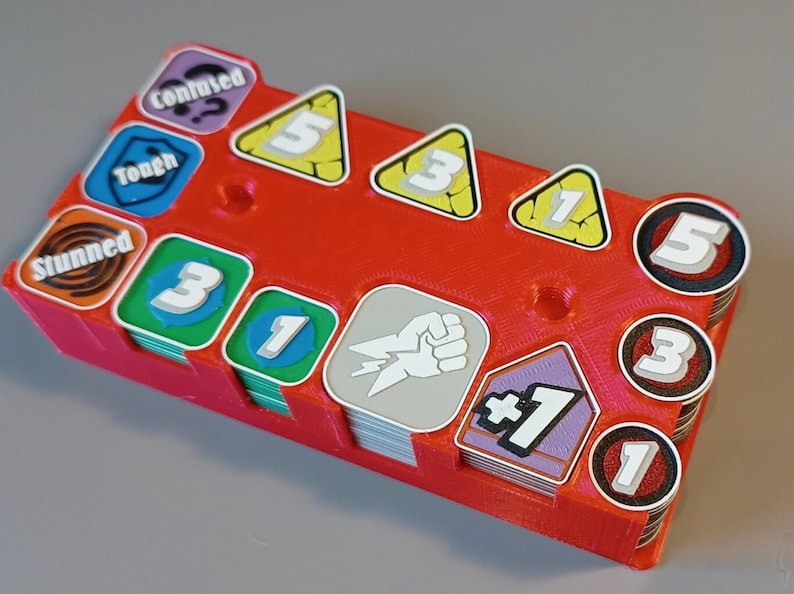 Puede incluir: Un organizador de pl&aacute;stico rojo con ranuras para guardar peque&ntilde;as piezas de juego. El organizador tiene una variedad de piezas de juego, incluyendo un pu&ntilde;o, un m&aacute;s uno, un n&uacute;mero uno, un n&uacute;mero tres y un n&uacute;mero cinco.