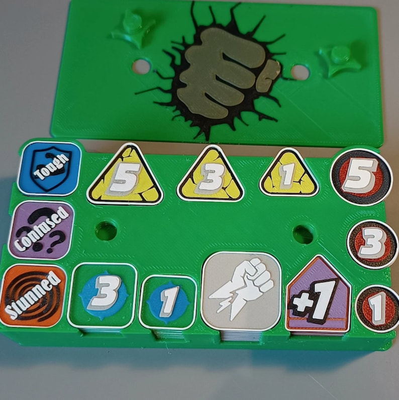 Puede incluir: Un tablero de juego de pl&aacute;stico verde con un gr&aacute;fico de pu&ntilde;o y varias fichas. Las fichas incluyen n&uacute;meros, s&iacute;mbolos y texto como "Tough", "Confused", "Stunned" y " +1".