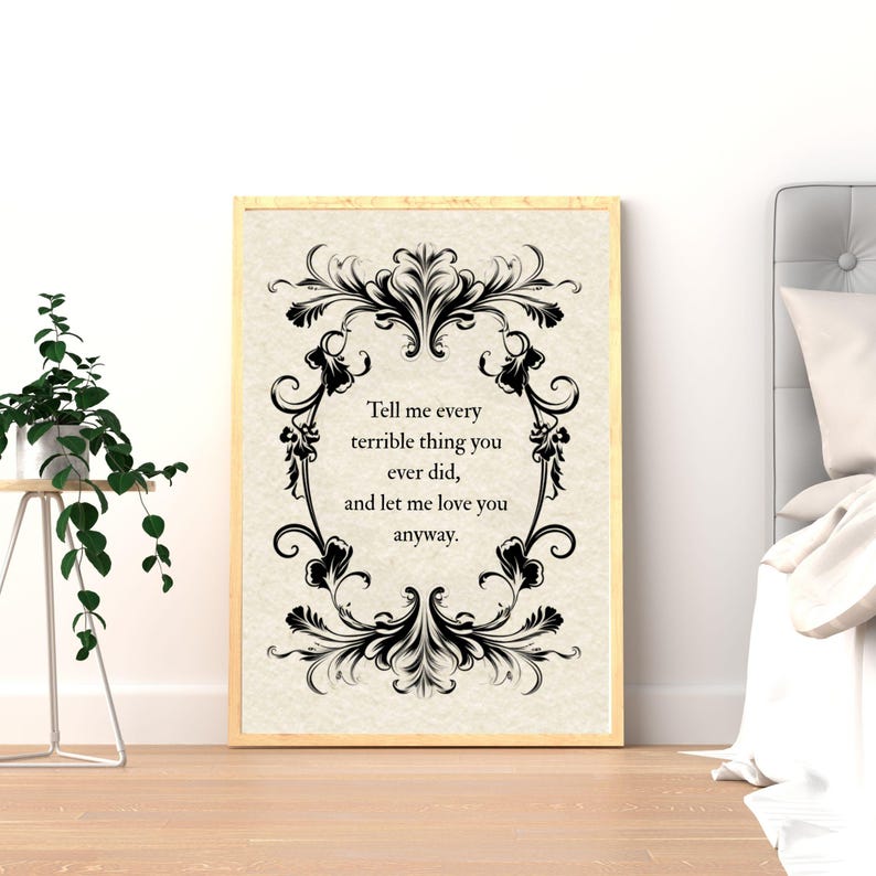 May include: A rectangular wall art print in a light wood frame featuring a cream-colored background with a black ornate filigree border. The text in the center reads: Tell me every terrible thing you ever did, and let me love you anyway.