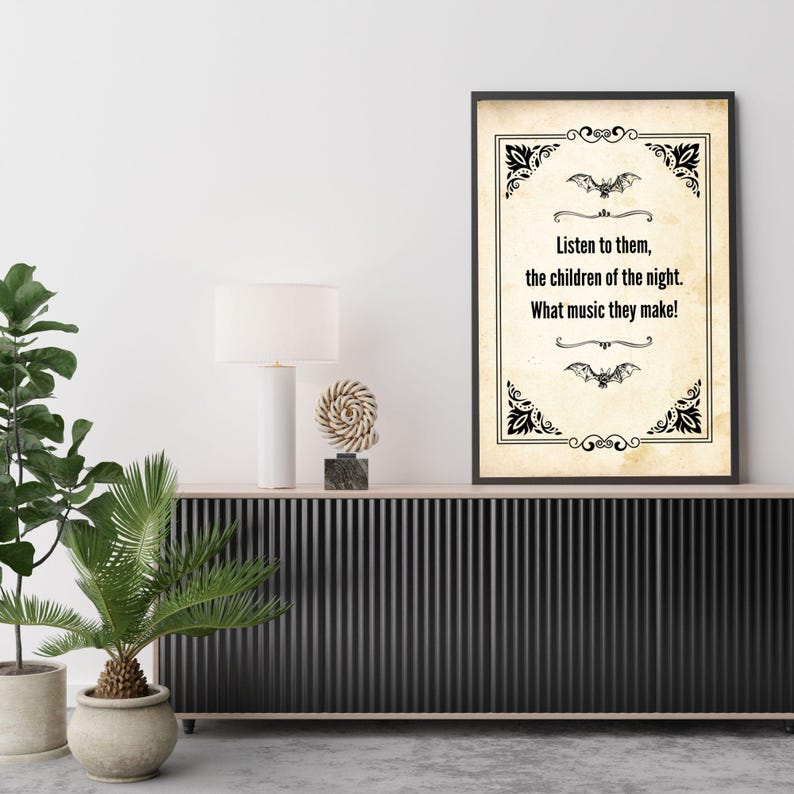 May include: A framed print with a vintage parchment background and black decorative borders. The text reads, "Listen to them, the children of the night. What music they make!" Two bat illustrations are above and below the text. The print is displayed on a black cabinet.