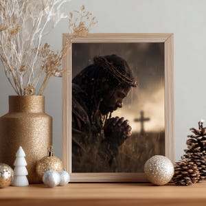 May include: A framed print depicting a person with dreadlocks wearing a crown of thorns, shown in profile with hands clasped in prayer. The scene is set outdoors in a field during rain, with a silhouette of a cross visible in the background.