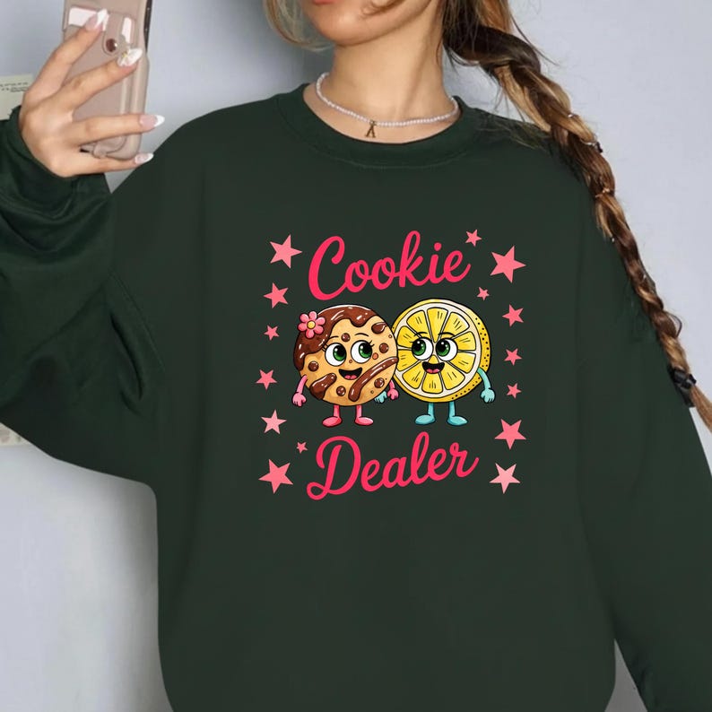 Sweatshirt featuring a cute cartoon cookie and lemon characters holding hands with the text “Cookie Dealer,” shown in a playful, colorful design; the design is available on t-shirts and sweatshirts in multiple sizes and a variety of colors.