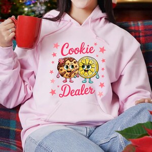 Sweatshirt featuring a cute cartoon cookie and lemon characters holding hands with the text “Cookie Dealer,” shown in a playful, colorful design; the design is available on t-shirts and sweatshirts in multiple sizes and a variety of colors.