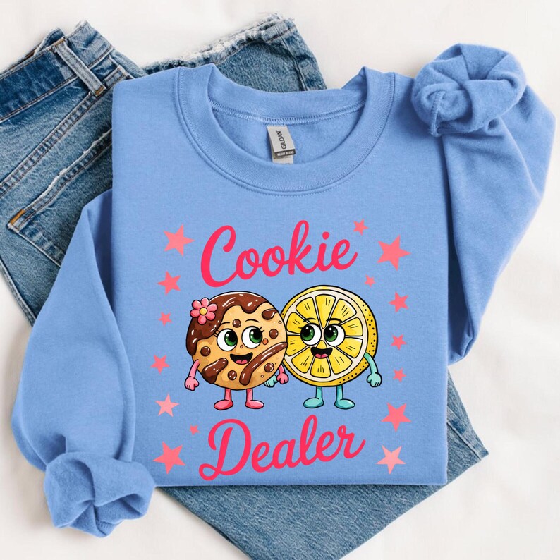 Sweatshirt featuring a cute cartoon cookie and lemon characters holding hands with the text “Cookie Dealer,” shown in a playful, colorful design; the design is available on t-shirts and sweatshirts in multiple sizes and a variety of colors.