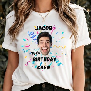 Puede incluir: Camiseta blanca con un gráfico que presenta una cara sonriente, el nombre "Jacob" y el texto "35th BIRTHDAY CREW". El diseño incluye confeti y serpentinas de colores, creando un aspecto festivo.