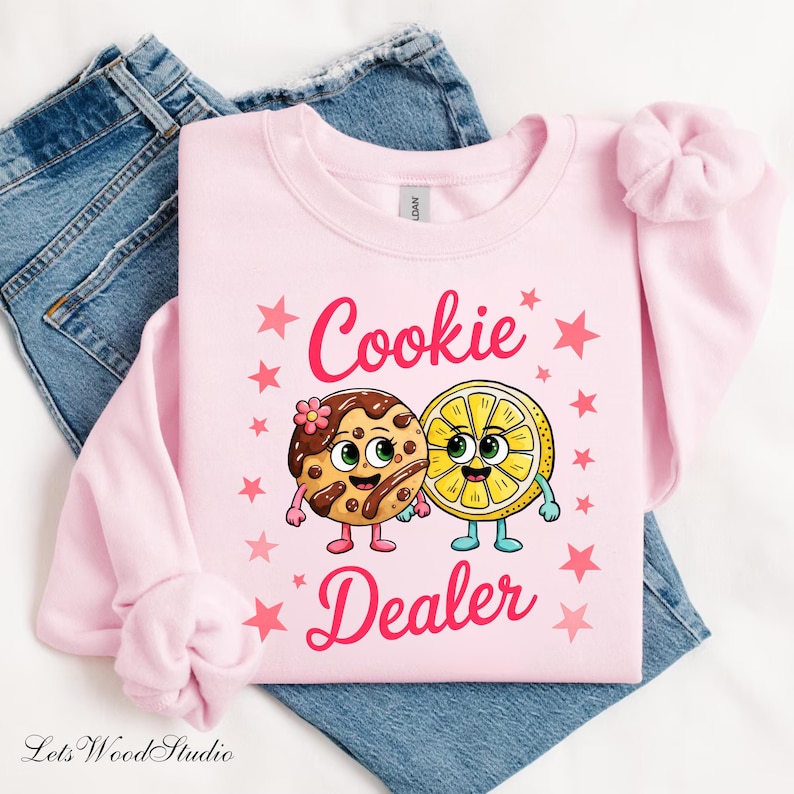 Sweatshirt featuring a cute cartoon cookie and lemon characters holding hands with the text “Cookie Dealer,” shown in a playful, colorful design; the design is available on t-shirts and sweatshirts in multiple sizes and a variety of colors.