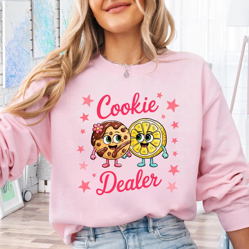Sweatshirt featuring a cute cartoon cookie and lemon characters holding hands with the text “Cookie Dealer,” shown in a playful, colorful design; the design is available on t-shirts and sweatshirts in multiple sizes and a variety of colors.