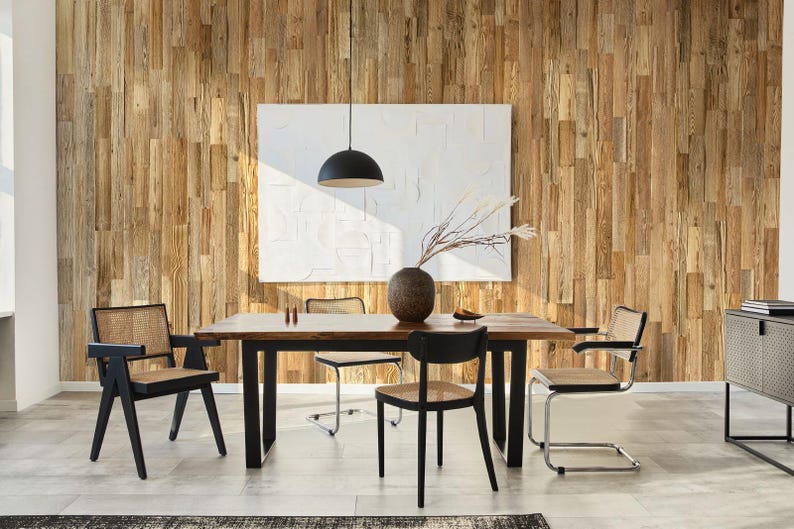 May include: A dining room scene featuring a dark wood table with black legs and several chairs. The chairs have woven seats and backs. A large white abstract artwork hangs on a wood plank wall. A black pendant light hangs above the table.