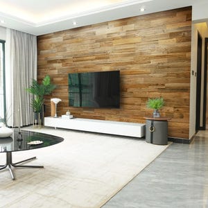 May include: A modern living room featuring a large flat-screen TV mounted on a wooden plank wall. A white entertainment console, a black glass coffee table, and a gray rug complete the space. Decorative plants and a side table add to the decor.