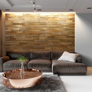 May include: A modern living room featuring a brown sectional sofa with a white pillow, a round coffee table with a copper-colored rim, and a wooden accent wall. A gray rug and curtains add to the room's decor.