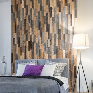 Könnte beinhalten: Ein graues Bett mit einem grauen und weiß gemusterten Kopfteil und einer grauen Bettdecke. Das Bett hat ein lila Kissen und zwei weiße Kissen. Das Bett steht vor einer Wand mit einer Holzverkleidung als Akzentwand. In der Ecke des Raumes steht eine Stehlampe mit einem weißen Lampenschirm.