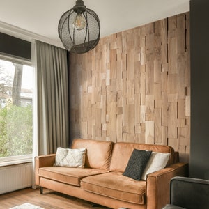 May include: A brown leather sofa with three pillows sits in front of a wall covered in wood panels. The panels are arranged in a random pattern and are a light brown color. A black metal light fixture hangs from the ceiling above the sofa.