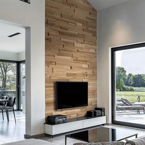 May include: A modern living room with a large flat screen TV mounted on a wall with wood paneling. The room has a large window with a view of a grassy field and a patio with lounge chairs. There is a gray couch with a black and white patterned pillow in front of a black coffee table.