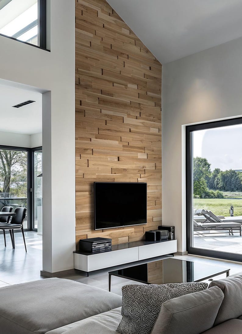 May include: A modern living room with a large flat screen TV mounted on a wall with wood paneling. The room has a large window with a view of a grassy field and a patio with lounge chairs. There is a gray couch with a black and white patterned pillow in front of a black coffee table.