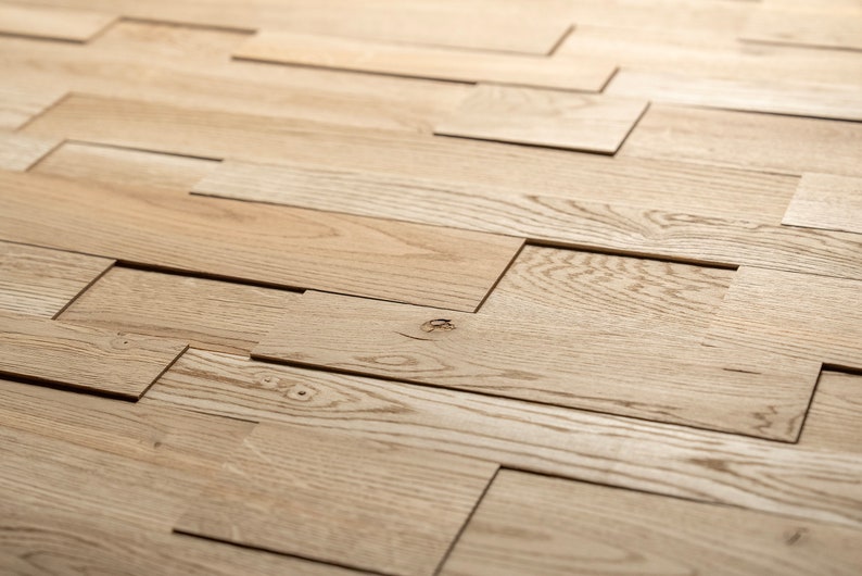 May include: A close-up of a wall made of light brown wood planks arranged in a staggered pattern. The planks are cut and arranged to create a unique and modern design.