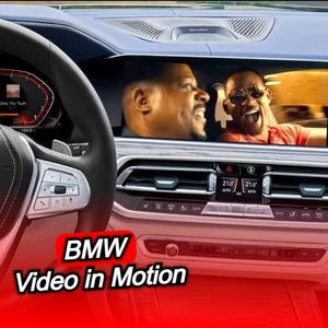 以下が含まれることがあります： BMWのダッシュボードのインテリアビュー。映画のシーンが表示されたスクリーン、ステアリングホイール、ダッシュボードが見え、赤いバナーに「BMW Video in Motion」の文字があります。