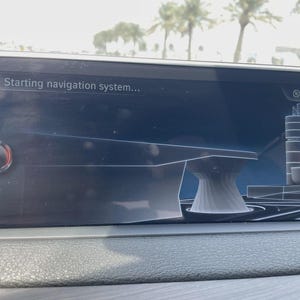 May include: A car's dashboard screen displays "Starting navigation system..." in white text. The screen shows a 3D architectural rendering and the time, 12:41 pm. The screen is set in a dark gray dashboard.