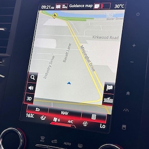 Op de afbeelding: Het scherm van het dashboard van een auto toont een navigatiekaart met straatnamen zoals Industry Drive en Kirkwood Road. Het scherm toont de tijd, de temperatuur in Celsius en verschillende bedieningspictogrammen. De kaart is licht van kleur.