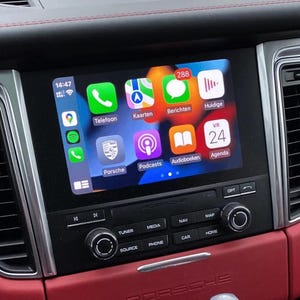 Könnte beinhalten: Der Bildschirm des Infotainmentsystems eines Autos zeigt App-Symbole wie Telefon, Karten und Podcasts. Die Uhrzeit wird mit 14:47 und eine Benachrichtigungsanzahl von 288 angezeigt. Das Armaturenbrett hat rotes Leder und silberne Zierleisten.