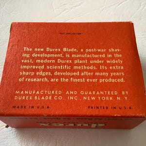 Może przedstawiać: Pomarańczowe, zabytkowe pudełko na ostrza Durex z białym tekstem. Tekst zawiera "The new Durex Blade" i "Made in U.S.A.". Pudełko jest prostokątne i wygląda na kartonowe.