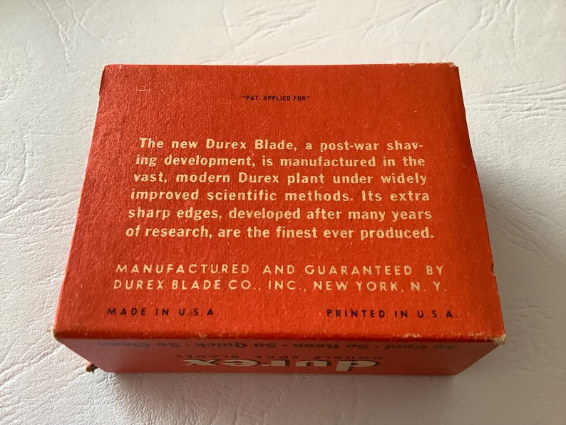 Może przedstawiać: Pomarańczowe, zabytkowe pudełko na ostrza Durex z białym tekstem. Tekst zawiera "The new Durex Blade" i "Made in U.S.A.". Pudełko jest prostokątne i wygląda na kartonowe.