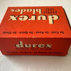 Może przedstawiać: Zabytkowe pudełko Durex Double Edge Blades. Pudełko jest w żywym czerwonym kolorze z nazwą marki w pogrubionej, białej czcionce. Tekst na pudełku brzmi "So Cool - So Keen - So Quick - So Clean". Pudełko jest lekko zużyte, co sugeruje jego wiek.