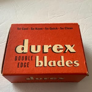 Może przedstawiać: Vintage pomarańczowe pudełko z ostrzami Durex Double Edge. Pudełko zawiera nazwę marki dużymi, pogrubionymi, kremowymi literami, ze słowami "DOUBLE EDGE" i "blades" r&oacute;wnież w kolorze kremowym. Na g&oacute;rze pudełka widnieje napis "So Cool - So Keen - So Quick - So Clean."
