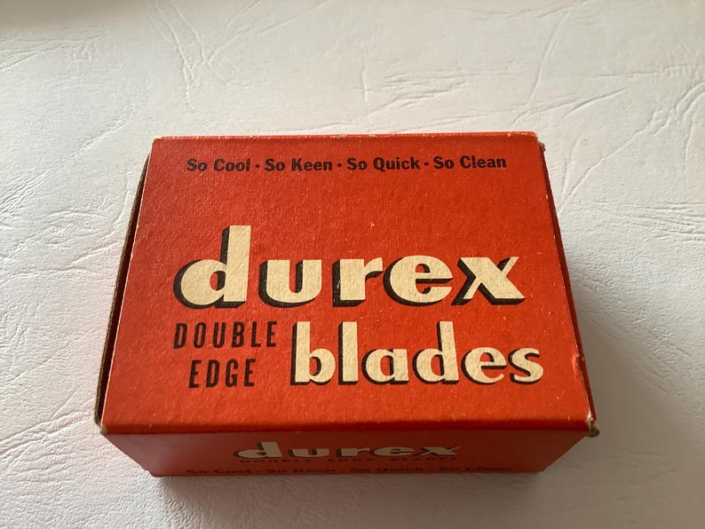 Może przedstawiać: Vintage pomarańczowe pudełko z ostrzami Durex Double Edge. Pudełko zawiera nazwę marki dużymi, pogrubionymi, kremowymi literami, ze słowami "DOUBLE EDGE" i "blades" r&oacute;wnież w kolorze kremowym. Na g&oacute;rze pudełka widnieje napis "So Cool - So Keen - So Quick - So Clean."