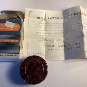 Könnte beinhalten: Vintage Rolls Razor Strop Dressing Kit. Das Set enthält eine Box mit Text, einen runden Behälter mit dunklem, meliertem Muster und ein ungefaltetes Anleitungsblatt. Hergestellt in England.