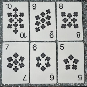 May include: A set of nine white playing cards with black clover symbols. The cards are numbered 5 through 10. The clover symbols are arranged in a star shape.