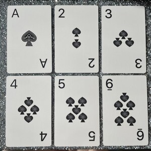 May include: A set of six playing cards featuring the suit of spades. The cards are numbered 1 through 6, with the ace being the first card. The cards are white with black spades and black numbers.