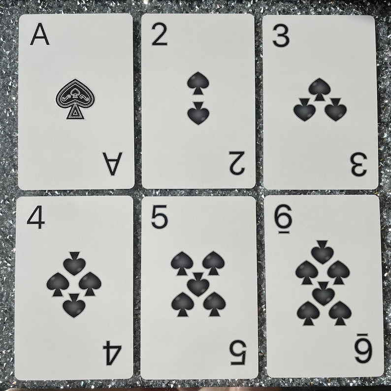 May include: A set of six playing cards featuring the suit of spades. The cards are numbered 1 through 6, with the ace being the first card. The cards are white with black spades and black numbers.