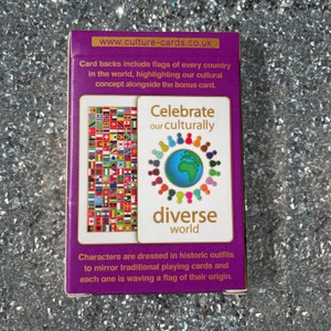 May include: A purple box with gold trim featuring a deck of playing cards. The box has the text "Celebrate our culturally diverse world" and shows a circle of people holding hands around a globe. The back of the cards features flags from around the world.