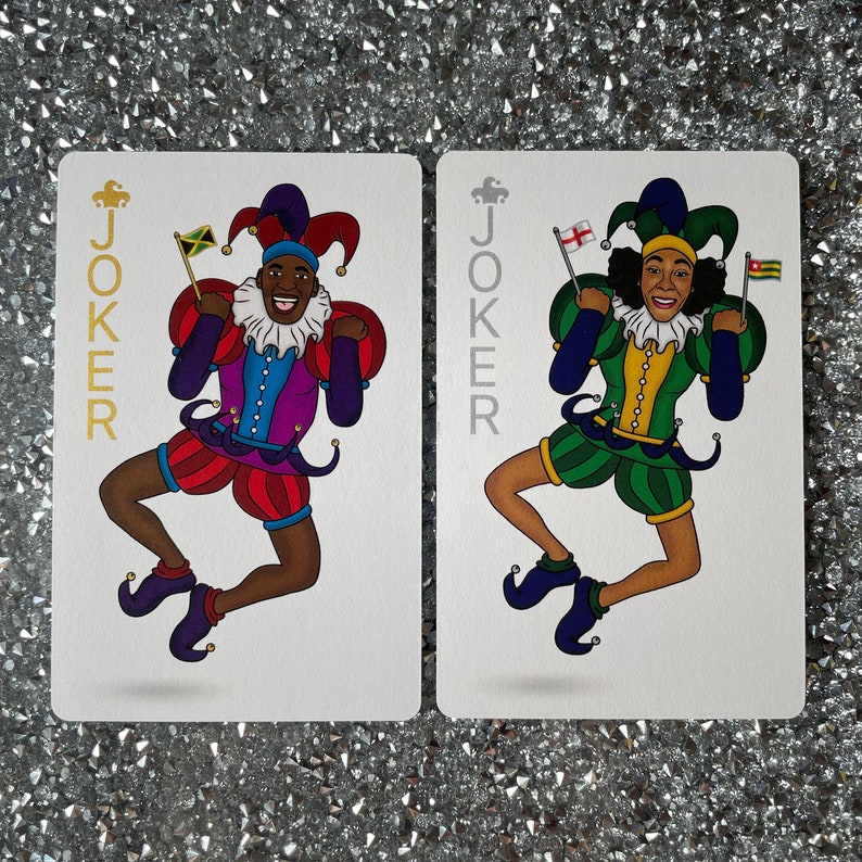 May include: Two playing cards with a joker design. The card on the left features a black and red jester with a green, yellow, and red hat. The card on the right features a black and green jester with a blue, yellow, and red hat. Both cards have the word "JOKER" printed in gold.