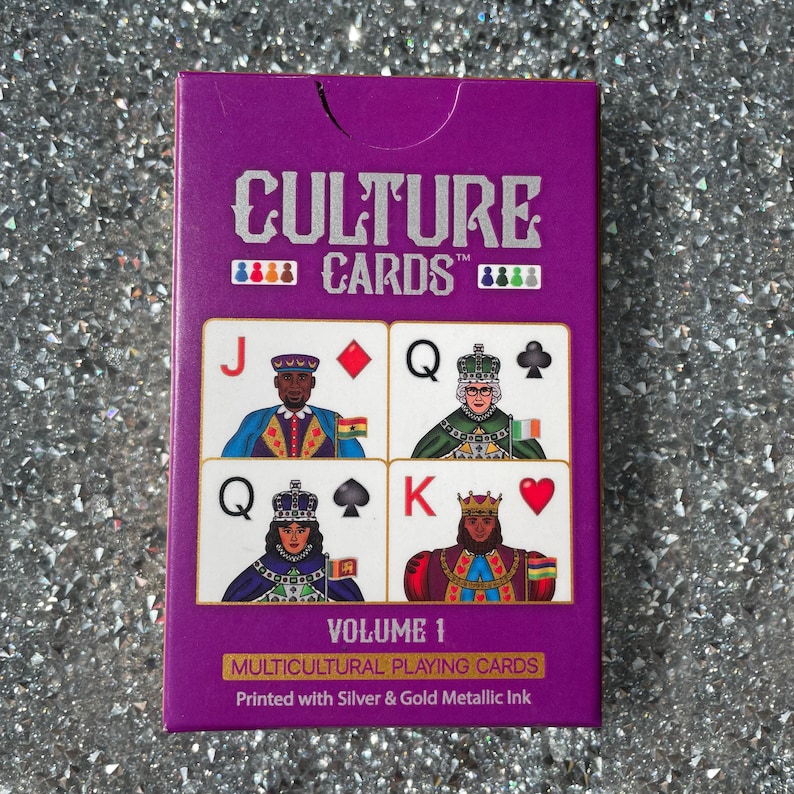 May include: A purple box of Culture Cards Volume 1 Multicultural Playing Cards. The box features a silver and gold metallic ink design with four playing cards: Jack of Diamonds, Queen of Clubs, Queen of Spades, and King of Hearts. Each card features a person of color in a royal costume.