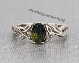 May include: A silver ring with a green oval gemstone set in a delicate, leafy design. The ring features two smaller diamonds on either side of the main stone.