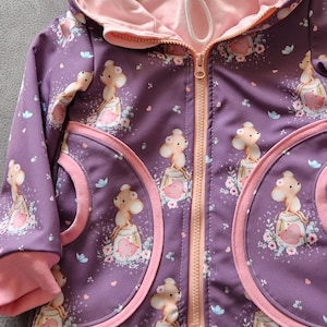 May include: A purple hooded jacket with a pink interior and trim. The jacket features a repeating pattern of a cartoon mouse in a jar with floral accents. The jacket has a full zip and two front pockets.