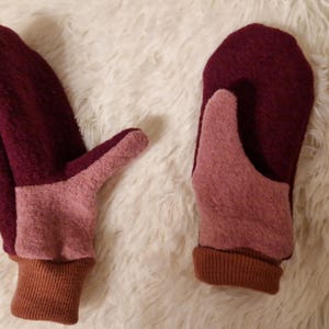 May include: A pair of burgundy and pink fleece mittens with brown cuffs. The mittens are made of a soft, fuzzy material and have a simple design.
