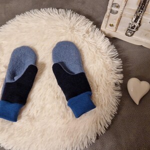 May include: A pair of blue and black fingerless mittens with a blue cuff. The mittens are on a white fluffy surface.