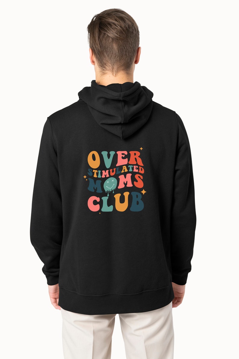 K&ouml;nnte beinhalten: Schwarzer Kapuzenpullover mit dem Text "OVERSTIMULATED MOMS CLUB" in einem Retro-Design. Das Design zeigt orange, rosa, blaue und gr&uuml;ne Schrift mit Sternakzenten. Der Hoodie hat eine Kapuze und lange &Auml;rmel.
