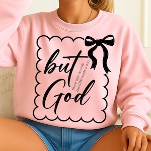 May include: A light pink crewneck sweatshirt featuring a black graphic design. The design includes a scalloped rectangular border, a black bow, and the text but God, there was no way, but GOD made a way in a mix of script and serif fonts.