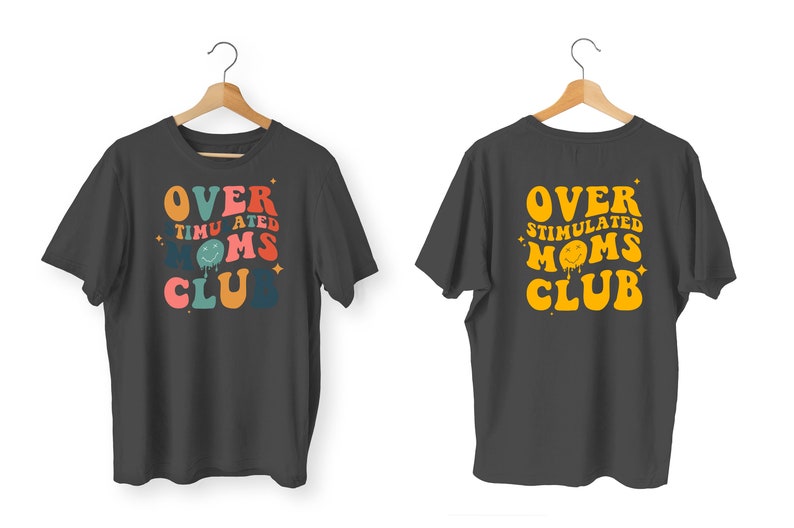 K&ouml;nnte beinhalten: Zwei anthrazitfarbene T-Shirts auf Holzb&uuml;geln. Die Vorderseite des ersten Shirts tr&auml;gt den Text "OVER STIMULATED MOMS CLUB" in Retro-Farben. Die R&uuml;ckseite des zweiten Shirts hat den gleichen Text in Gelb.