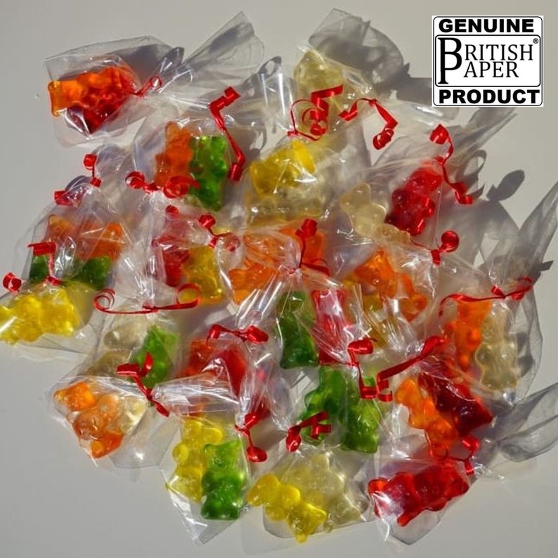 May include: A group of small, colourful gummy bears, each individually wrapped in clear cellophane bags and tied with red ribbon. The bags are arranged on a white surface. The image includes the text "GENUINE BRITISH PAPER PRODUCT".