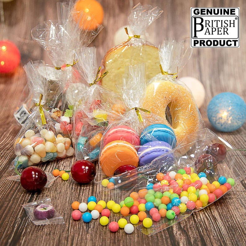 May include: An assortment of clear cellophane bags filled with various sweets, macarons, and a doughnut. The bags are tied with gold ribbon and the text "GENUINE BRITISH PAPER PRODUCT" is visible in the top right corner of the image.