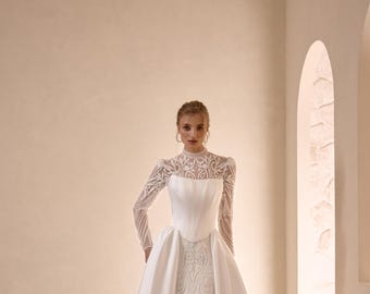 May include: A white wedding dress with a high, lace-trimmed neckline and long sleeves. The fitted bodice leads to a flowing skirt with a train. The dress features detailed embroidery and a satin overskirt.