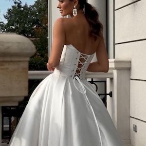 May include: A white strapless wedding dress with a lace-up back and a full skirt.