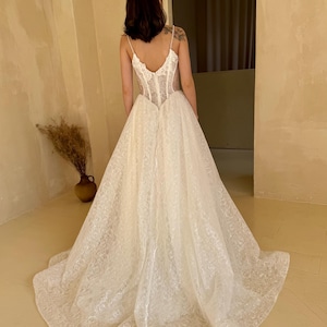 May include: A white wedding dress with a lace bodice and a flowing skirt. The dress has a low back and a fitted bodice.